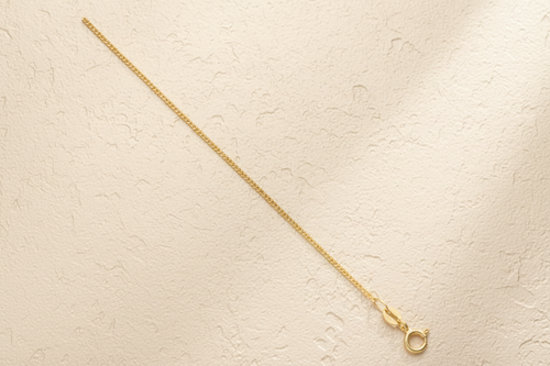 9ct Yellow Gold 1.1mm Classic Curb Chain on champagne textured background