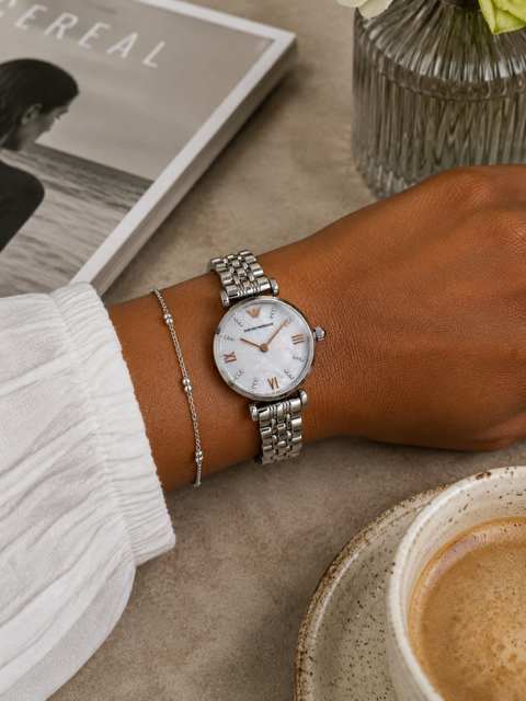 Silver watch on a wrist with a cup of coffee and magazine in the background