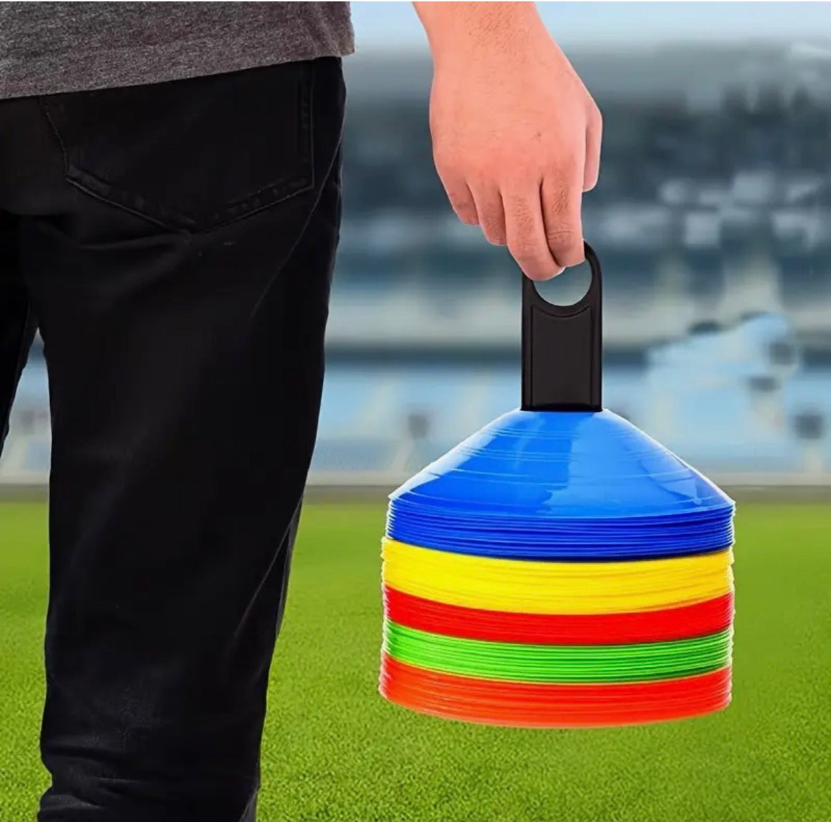 Person holding a stack of colorful training cones on a sports field