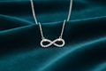 Silver CZ infinity pendant on deep teal velvet background