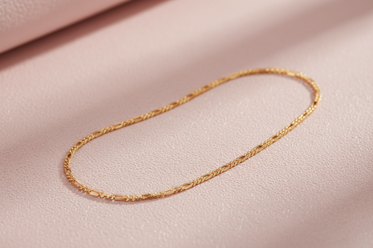 9ct Yellow Gold Figaro Anklet on soft pink textured background