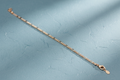 9ct Yellow Gold Rhodium Plated Figaro Anklet on dusty blue textured background